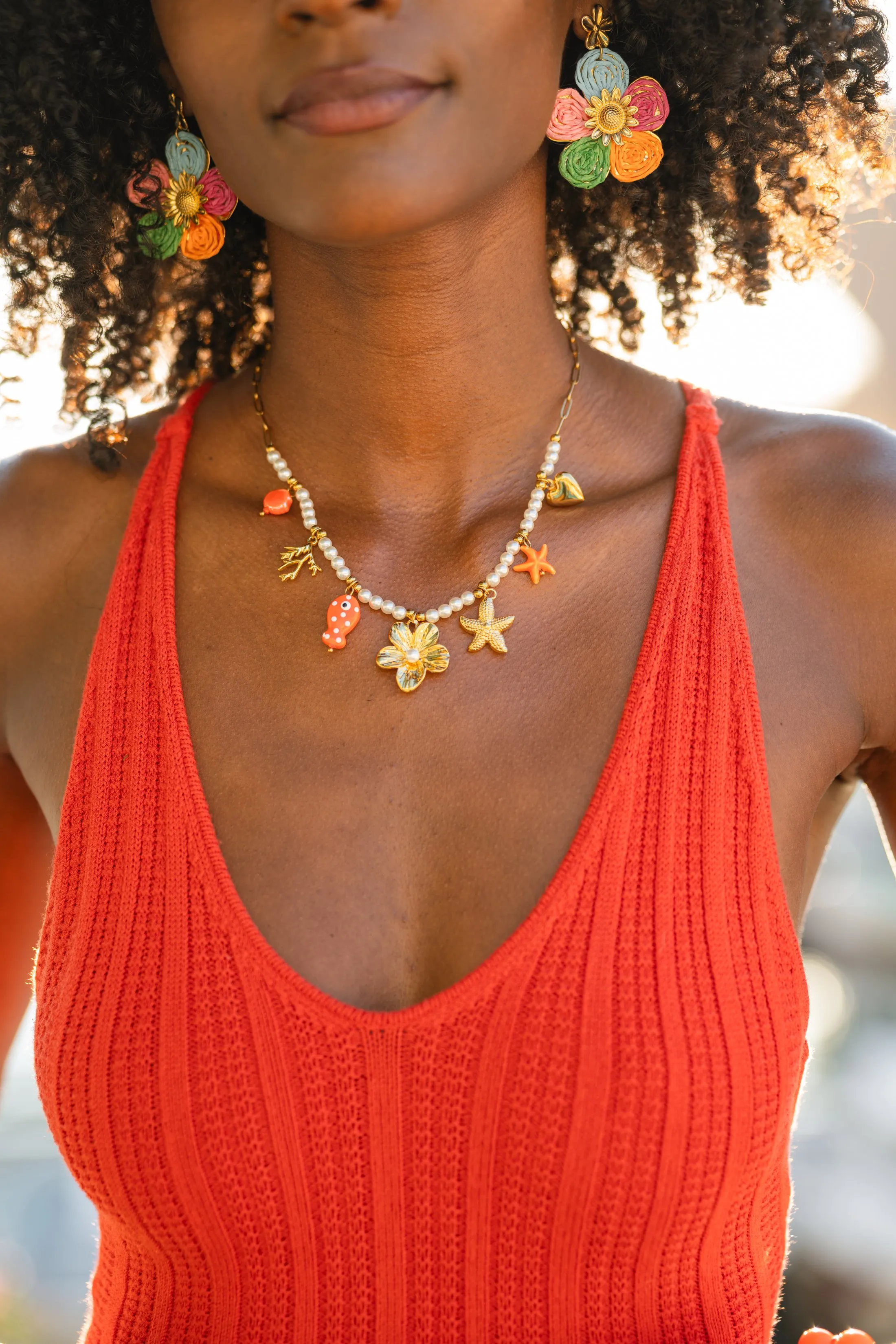 Collier de perles nacrées à breloques dorées fleur et étoiles de mer porté sur une robe corail, shooting Mary Jane à Marseille