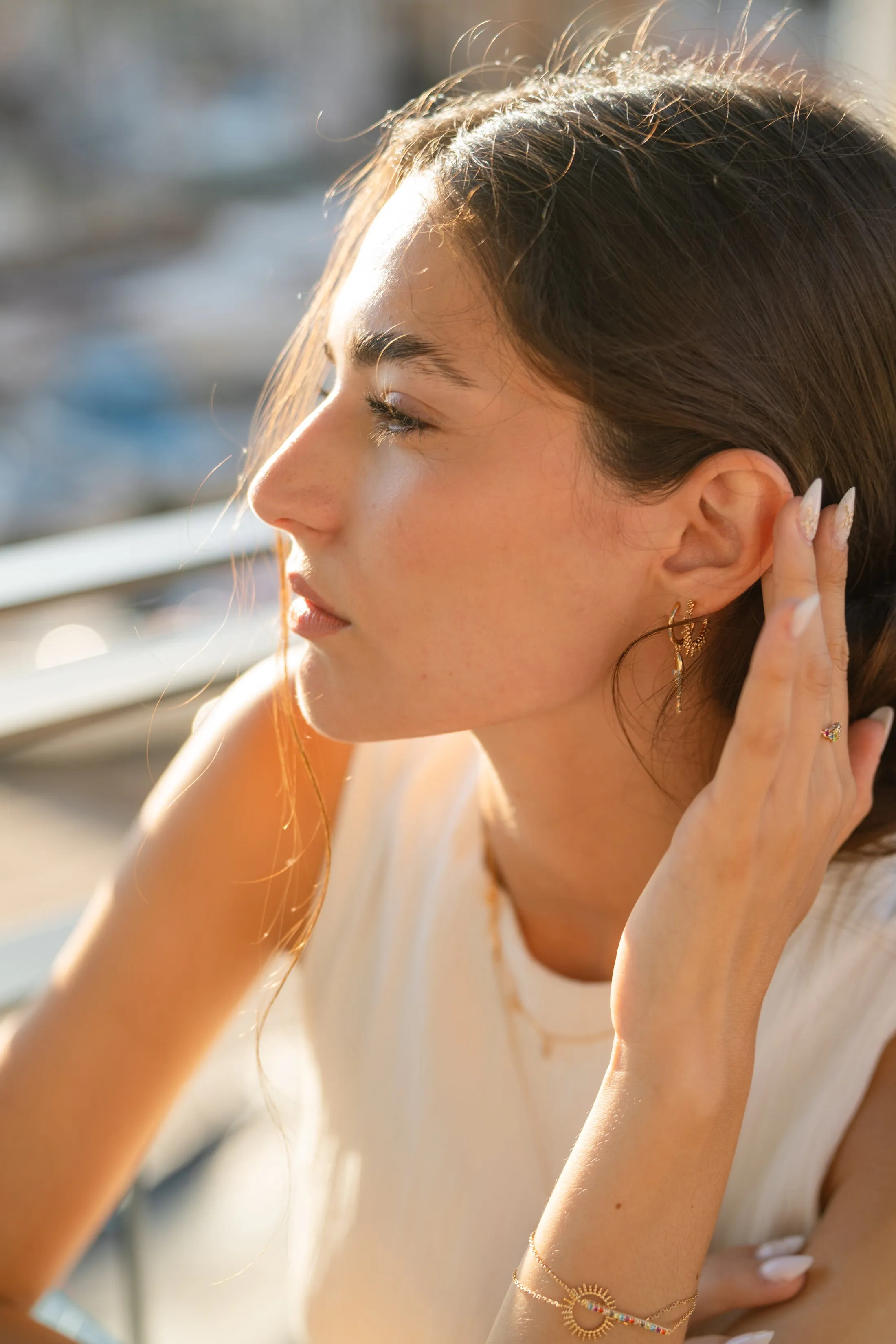 Profil d'une femme dégageant son oreille ornée de fines boucles d'oreilles pendantes à finition dorée, lumière du soir, shooting Mary Jane à Marseille